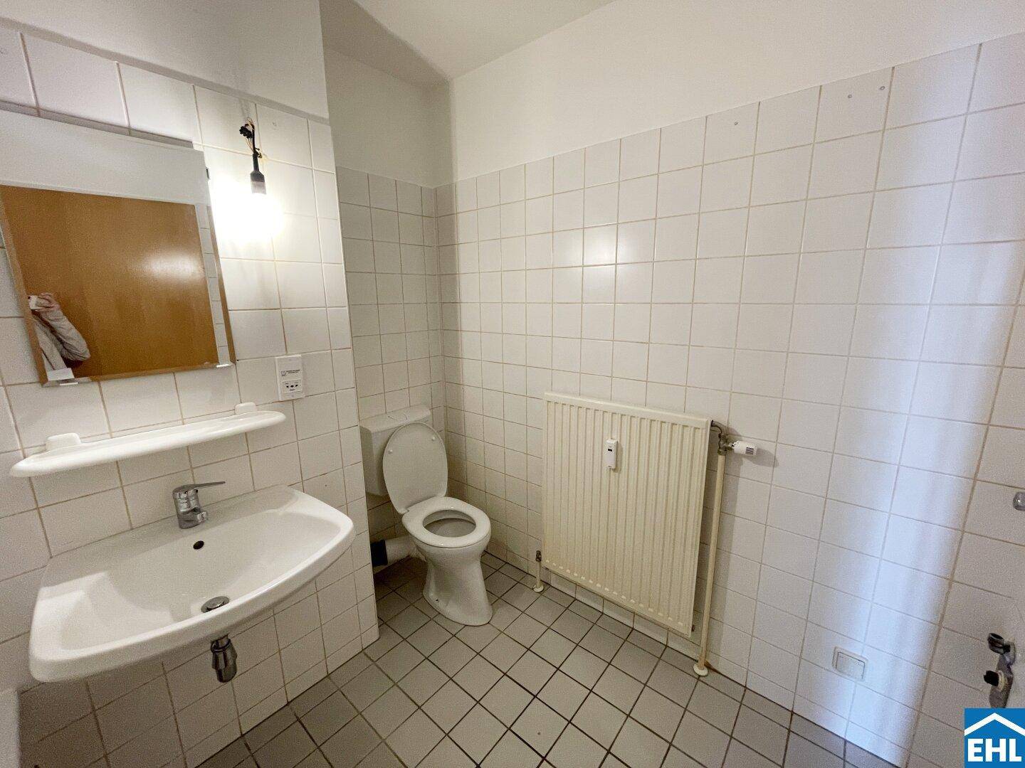Funktionales Badezimmer mit WC, Waschbecken und Heizkörper, vollständig gefliest.