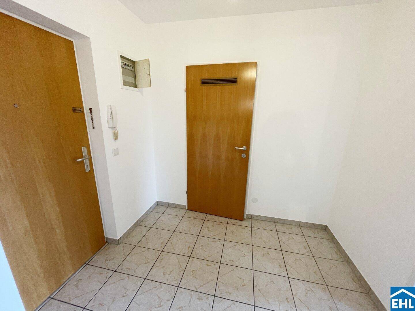 Eingangsbereich mit Fliesenboden und zwei Holztüren, bietet Zugang zur Wohnung.