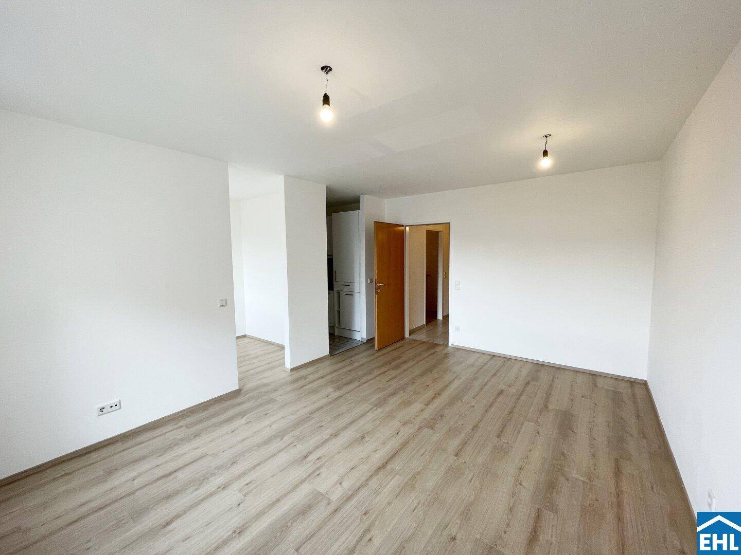 Geräumiges, helles Zimmer mit Laminatboden und Zugang zu weiteren Räumen.