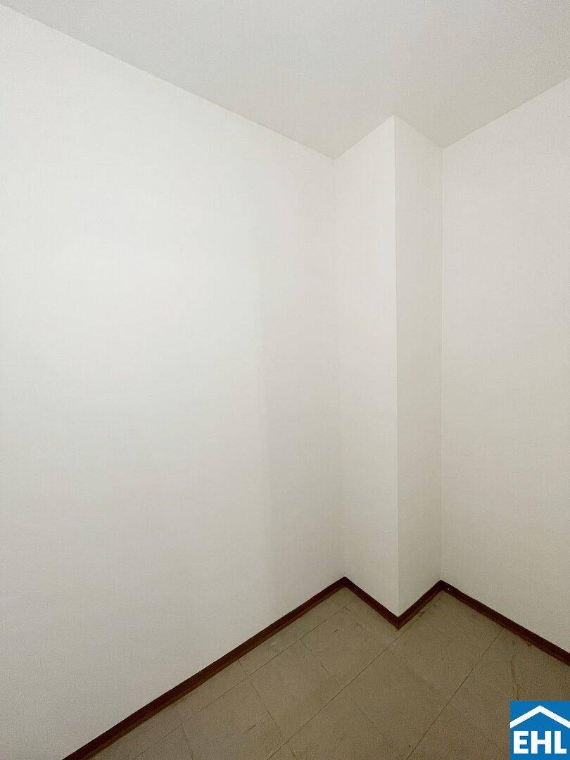 Ecke eines Raumes mit hellem Fliesenboden und weiß gestrichenen Wänden.