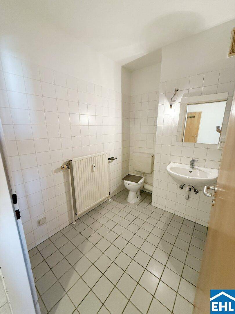 Kleines WC mit weißen Fliesen, Waschbecken und Heizkörper.
