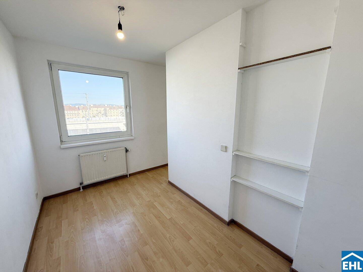 Helles Zimmer mit Laminatboden, Fenster und integriertem Regalbereich.