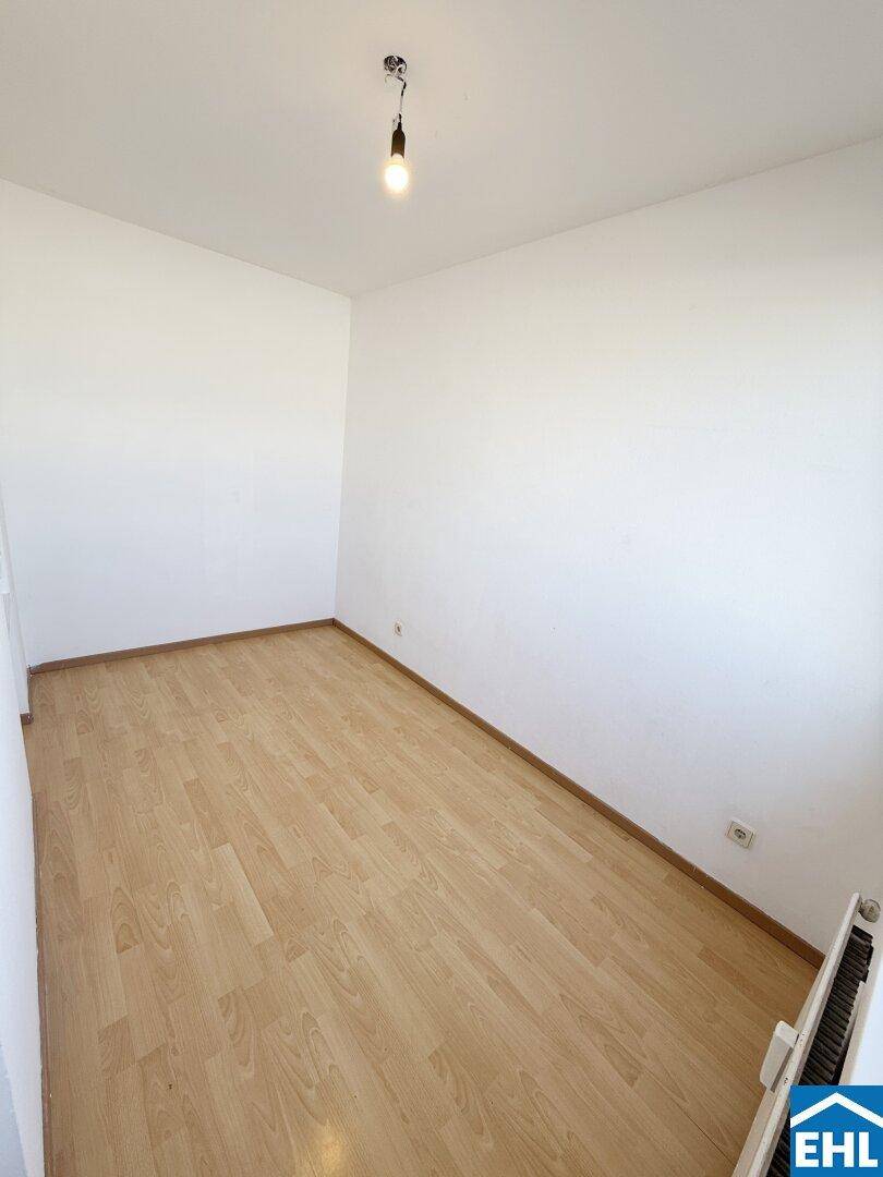 Leeres Zimmer mit Laminatboden und weiß gestrichenen Wänden, bereit zur individuellen Gestaltung.