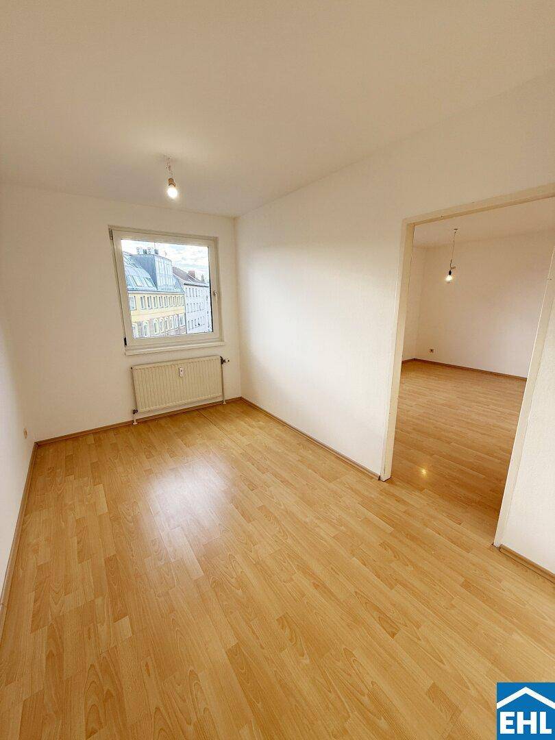 Helles Zimmer mit Parkettboden und Fenster, das viel Tageslicht hereinlässt.