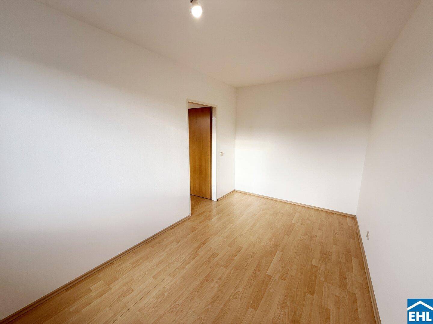 Leeres Zimmer mit hellem Parkettboden und Holztür, bereit zur individuellen Gestaltung.