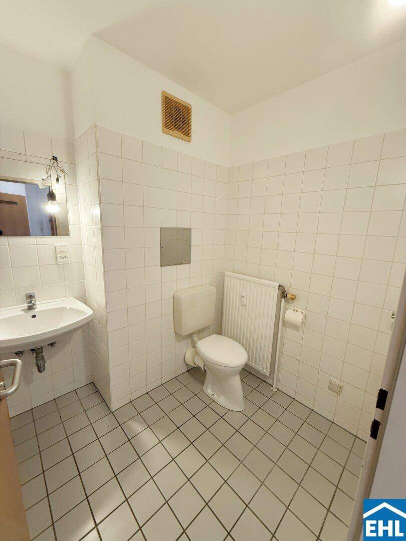 Separates WC mit Toilette, kleinem Waschbecken und weißen Wandfliesen.