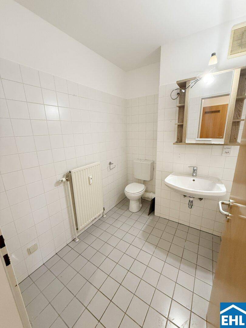 Helles Badezimmer mit WC, Waschbecken und Heizkörper, komplett gefliest in Weiß.
