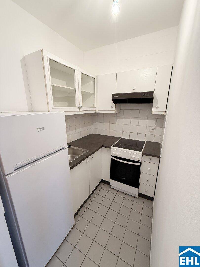 Funktionale Küche mit weißen Schränken, Fliesenboden und grundlegenden Geräten wie Kühlschrank und Herd.