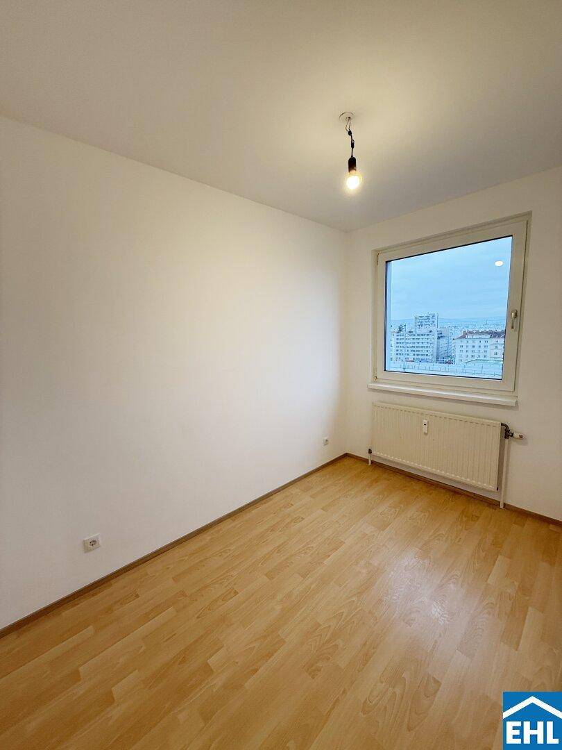 Kleiner, heller Raum mit Laminatboden und einem Fenster mit Blick auf die Stadt.
