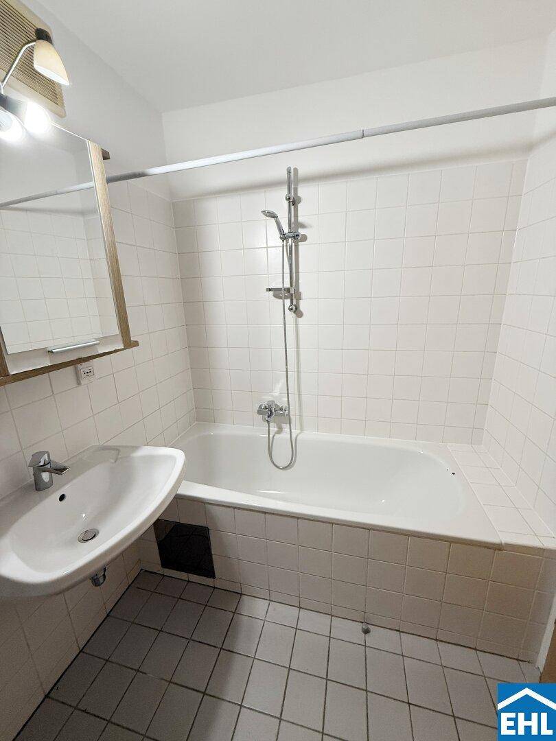 Gefliestes Badezimmer mit Badewanne und Duschvorrichtung, ausgestattet mit einem Waschbecken.