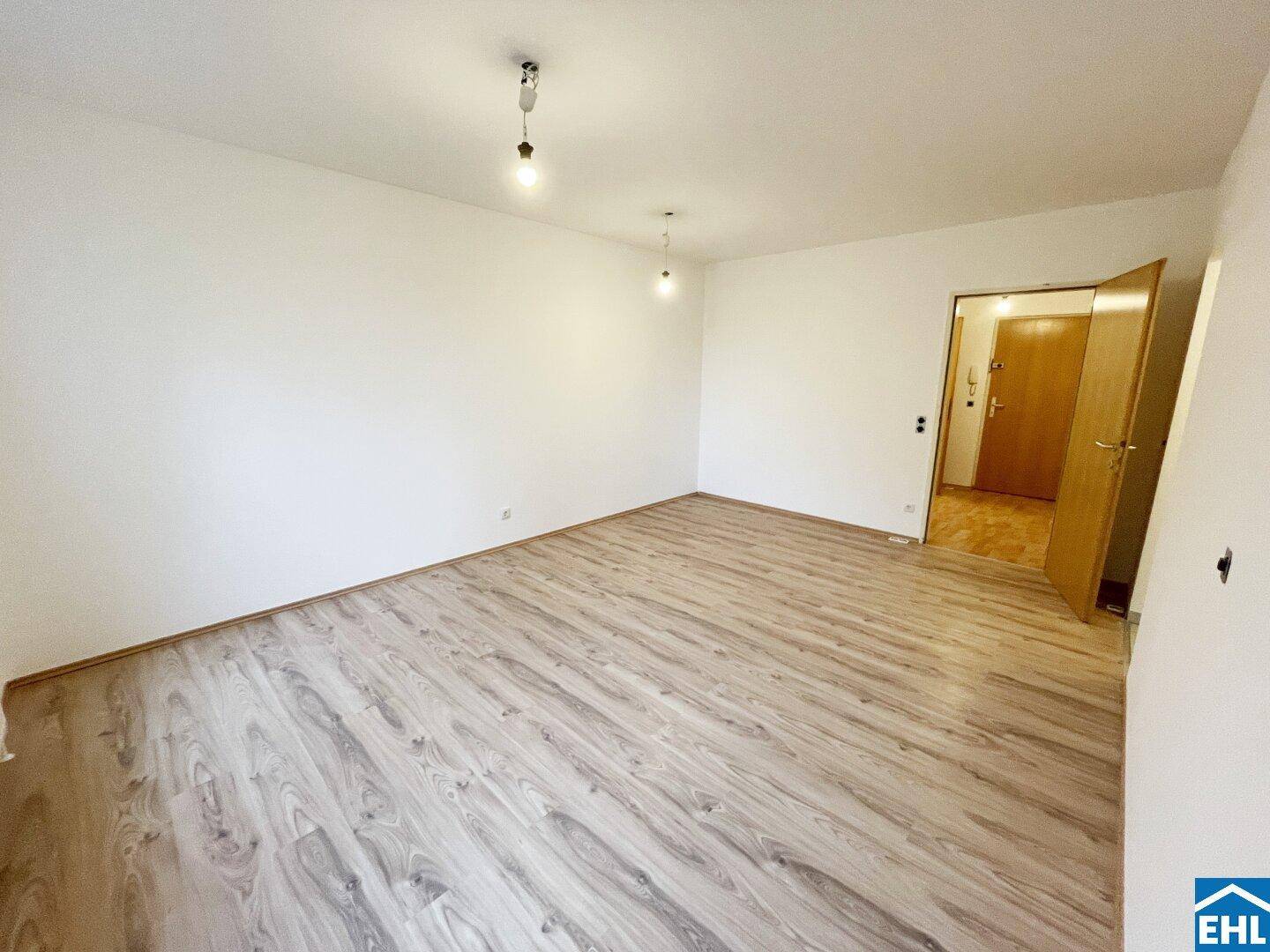 Geräumiger Wohnbereich mit hellem Laminatboden und Zugang zu weiteren Räumen.