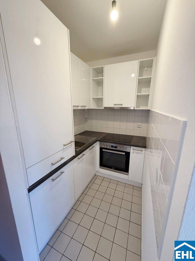 Kleine, moderne Küche mit weißen Hochglanzschränken, integriertem Backofen und Fliesenboden.