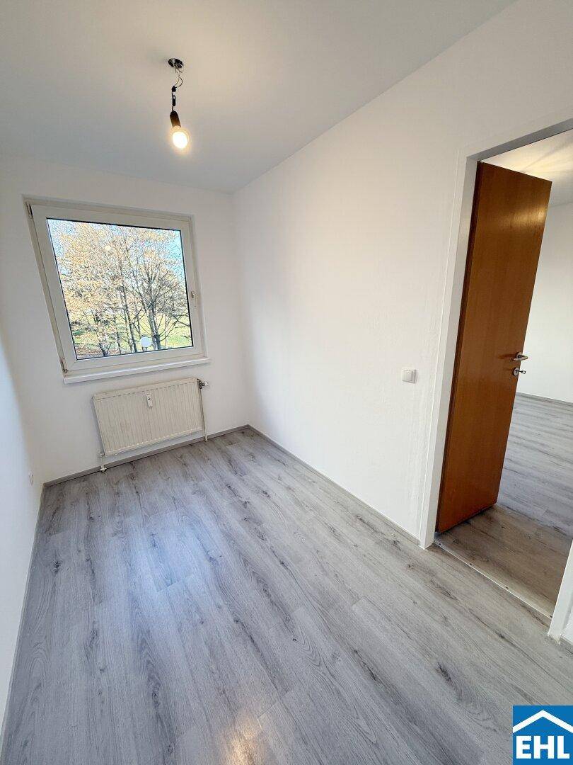 Helles Schlafzimmer mit Laminatboden und einem Fenster, das einen Blick ins Grüne bietet.