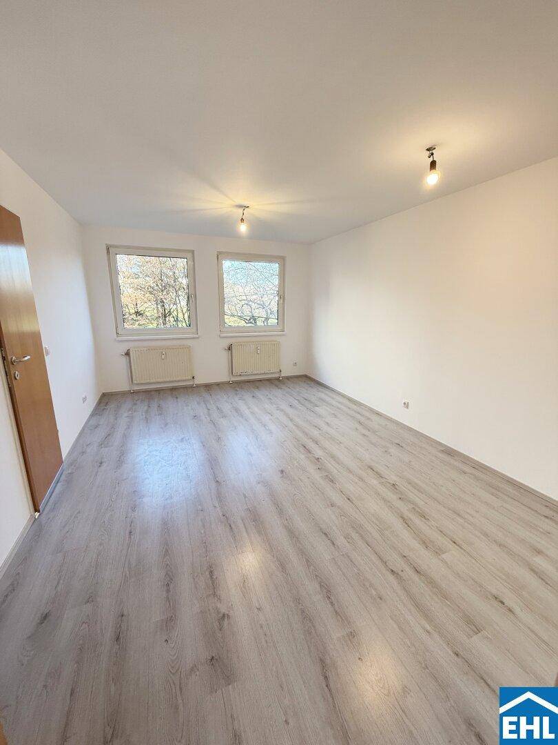 Geräumiges, helles Zimmer mit Laminatboden und zwei Fenstern, die viel Tageslicht hereinlassen.