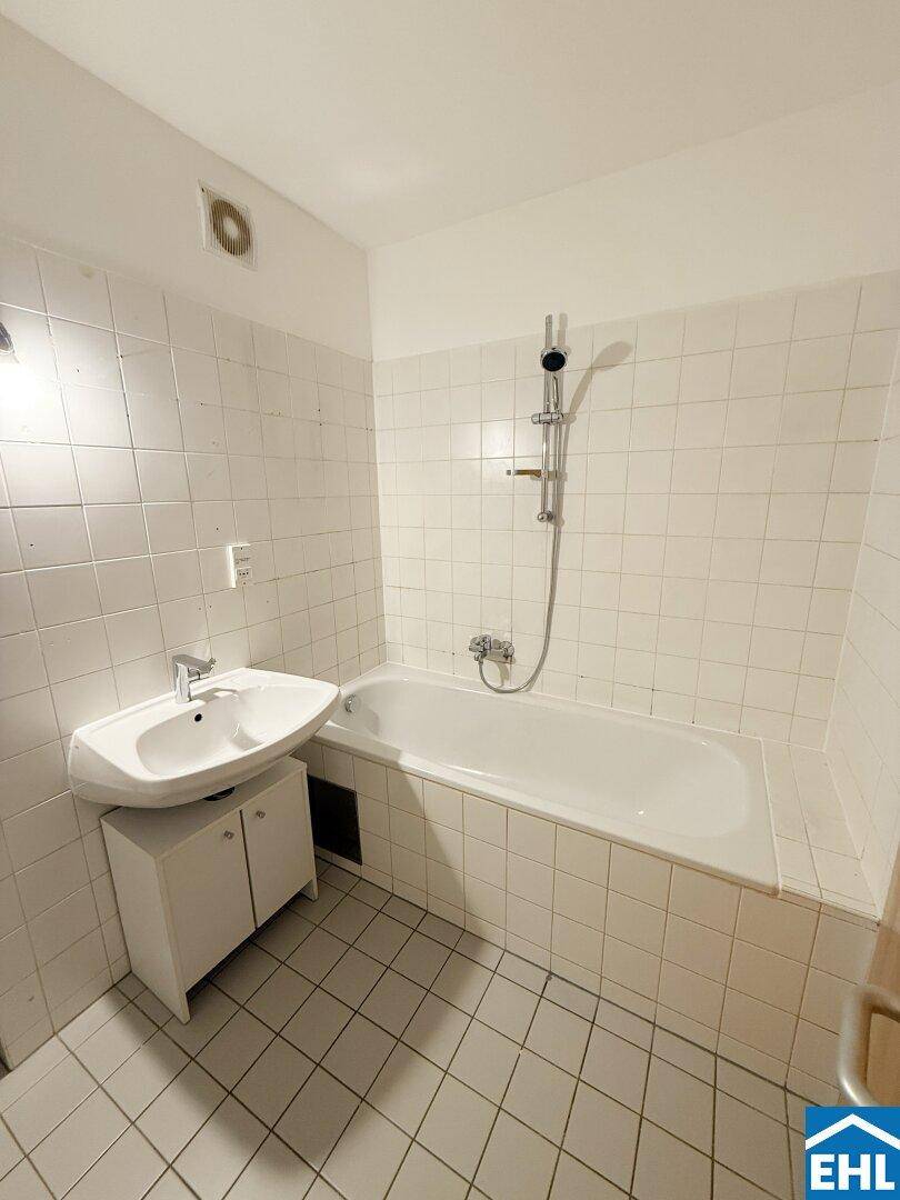 Gefliestes Badezimmer mit Badewanne, Waschbecken und Duscharmatur, in gutem Zustand.