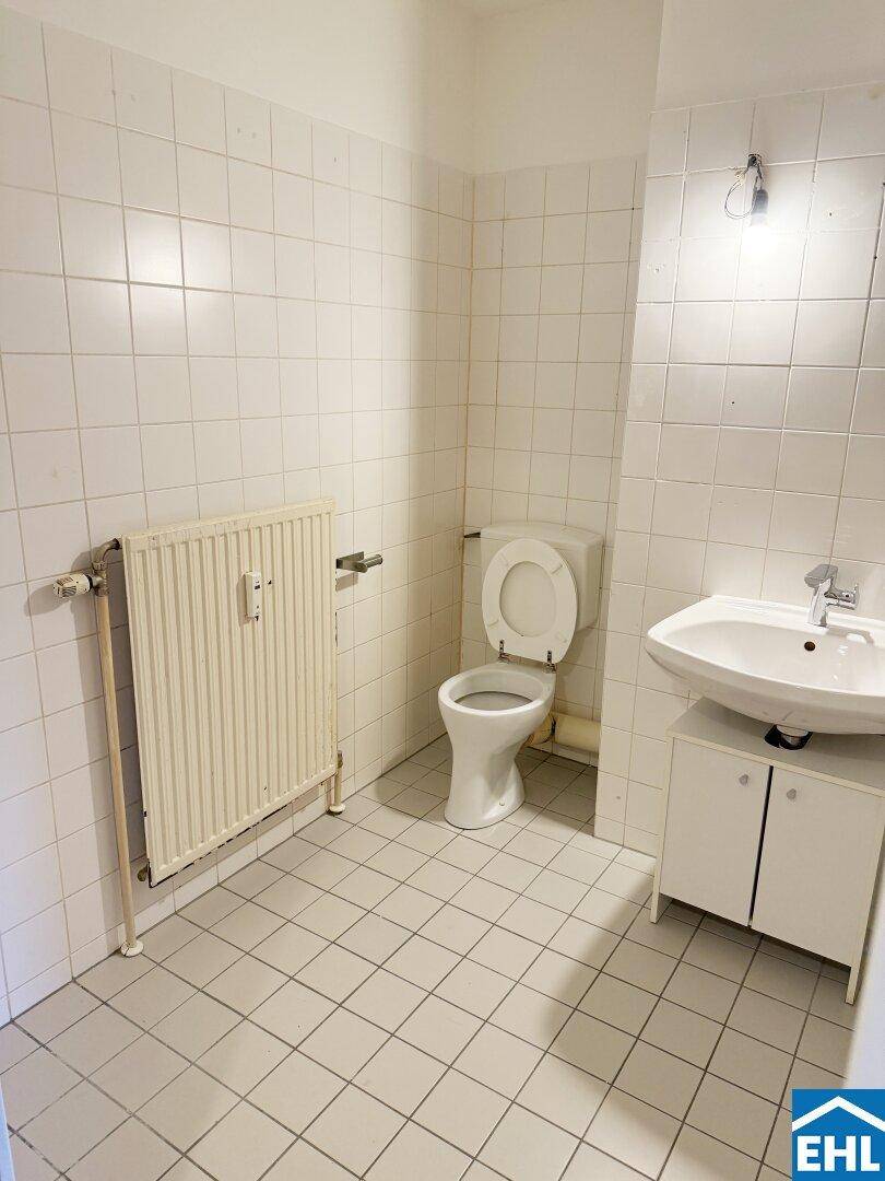 Separates WC mit Toilette, Waschbecken und Heizkörper, komplett gefliest.