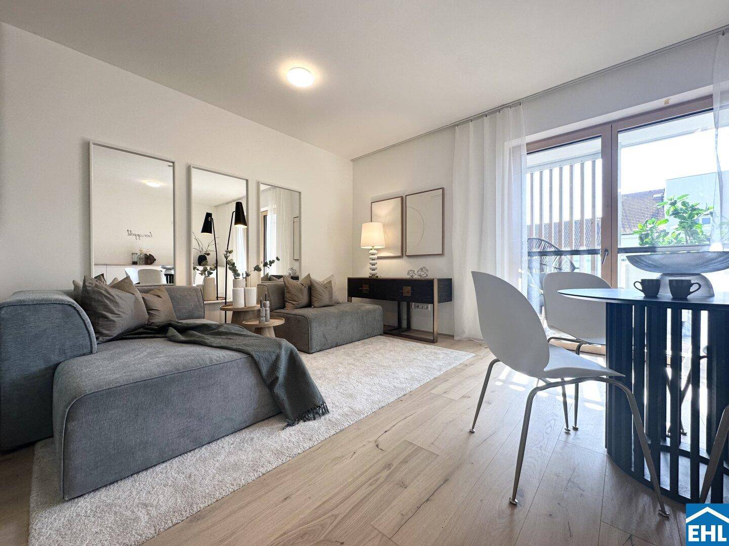Heller Wohn- und Essbereich mit Holzboden, modernem Sofa und kleinem Esstisch am Fenster.
