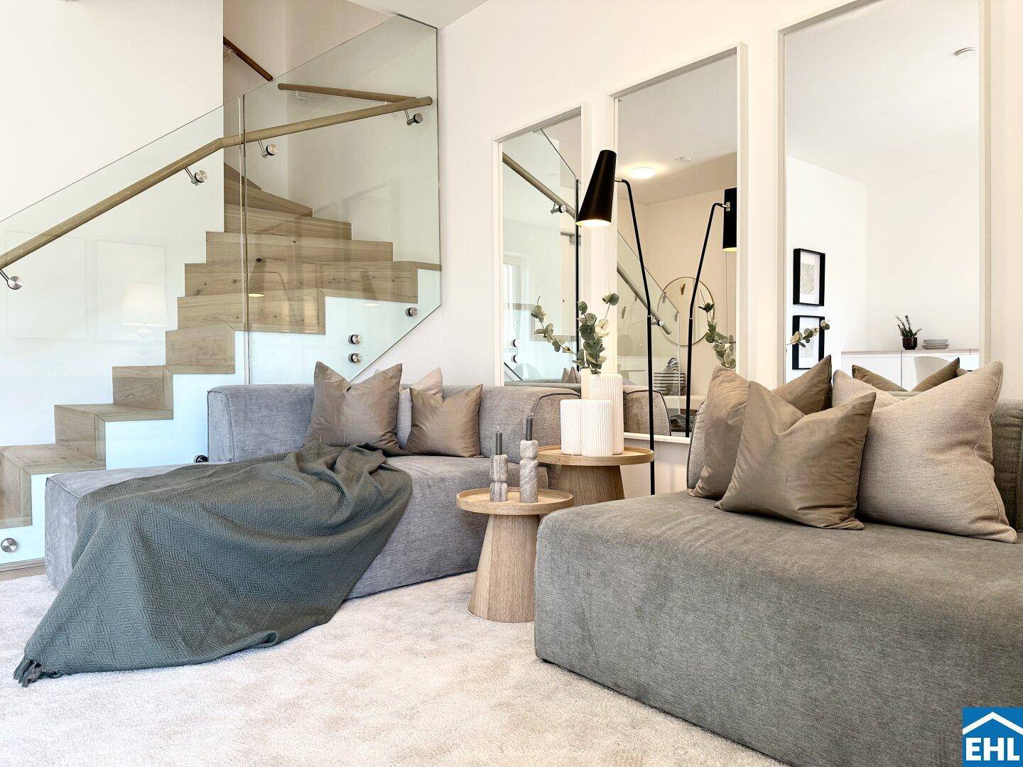 Detailansicht des Wohnbereichs mit bequemen Sofas und der eleganten Treppe mit Glasgeländer.