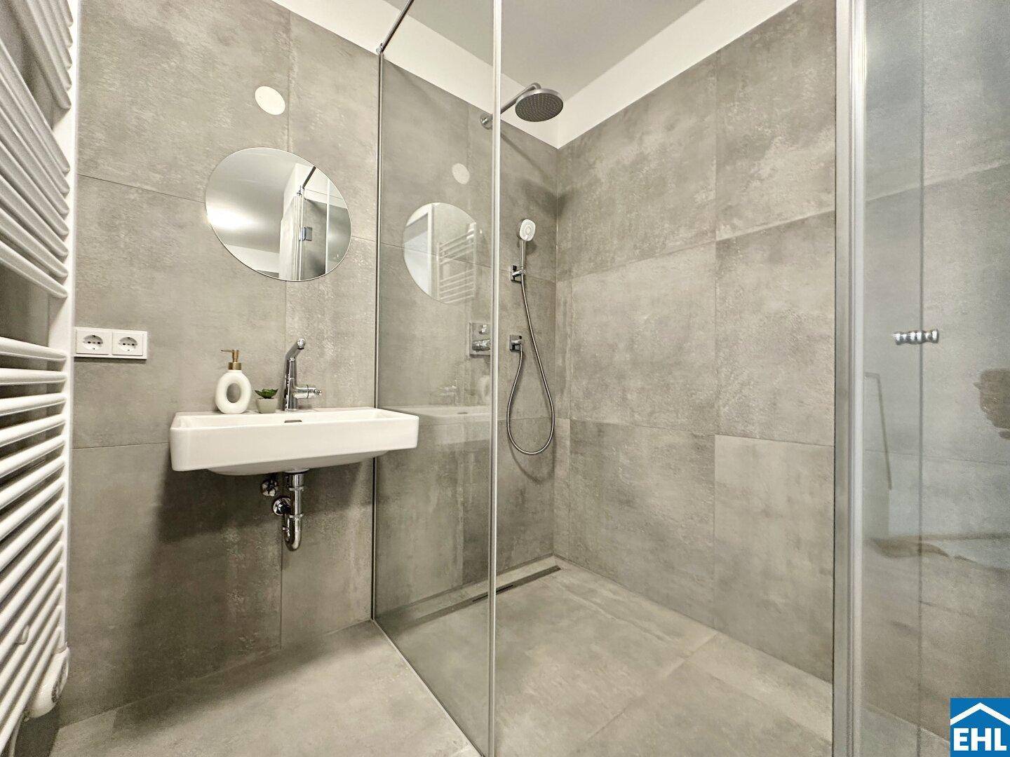 Modernes Badezimmer mit begehbarer Dusche, grauen Fliesen und kleinem Waschbecken.