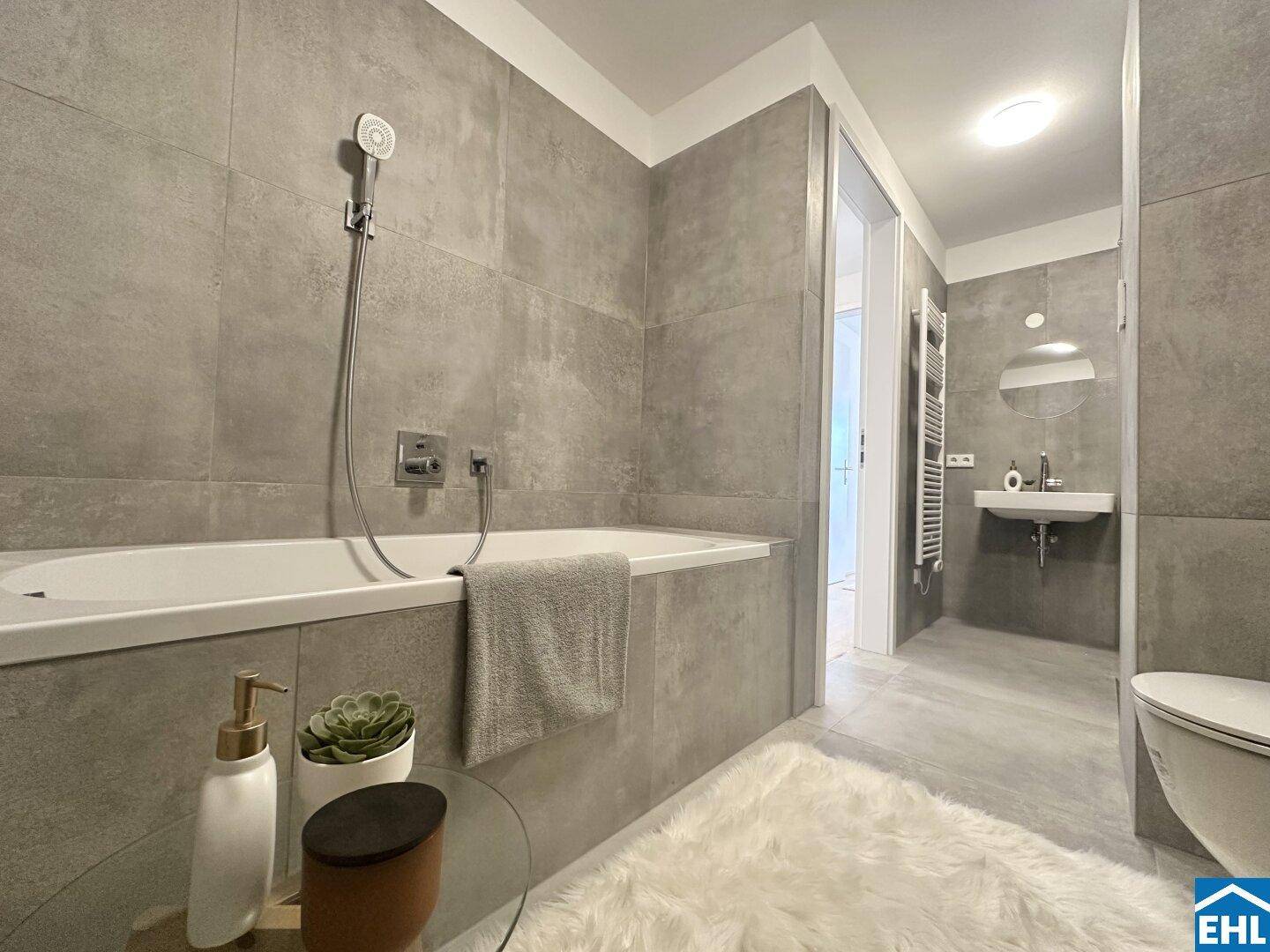 Modernes Badezimmer mit grauen Fliesen, Badewanne und wandhängendem WC.