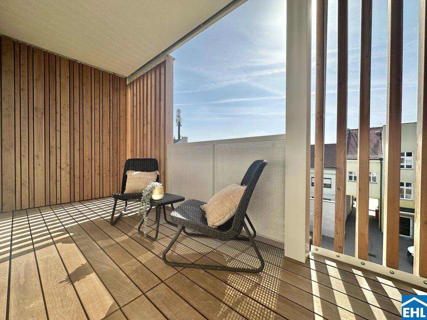 Sonniger Balkon mit Holzverkleidung, bequemen Stühlen und Blick auf die Umgebung.