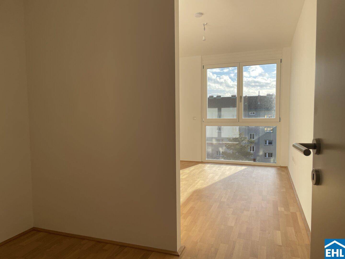 Lichtdurchflutetes Zimmer mit Parkettboden und großem Fenster, ideal für Schlaf- oder Arbeitsbereich.