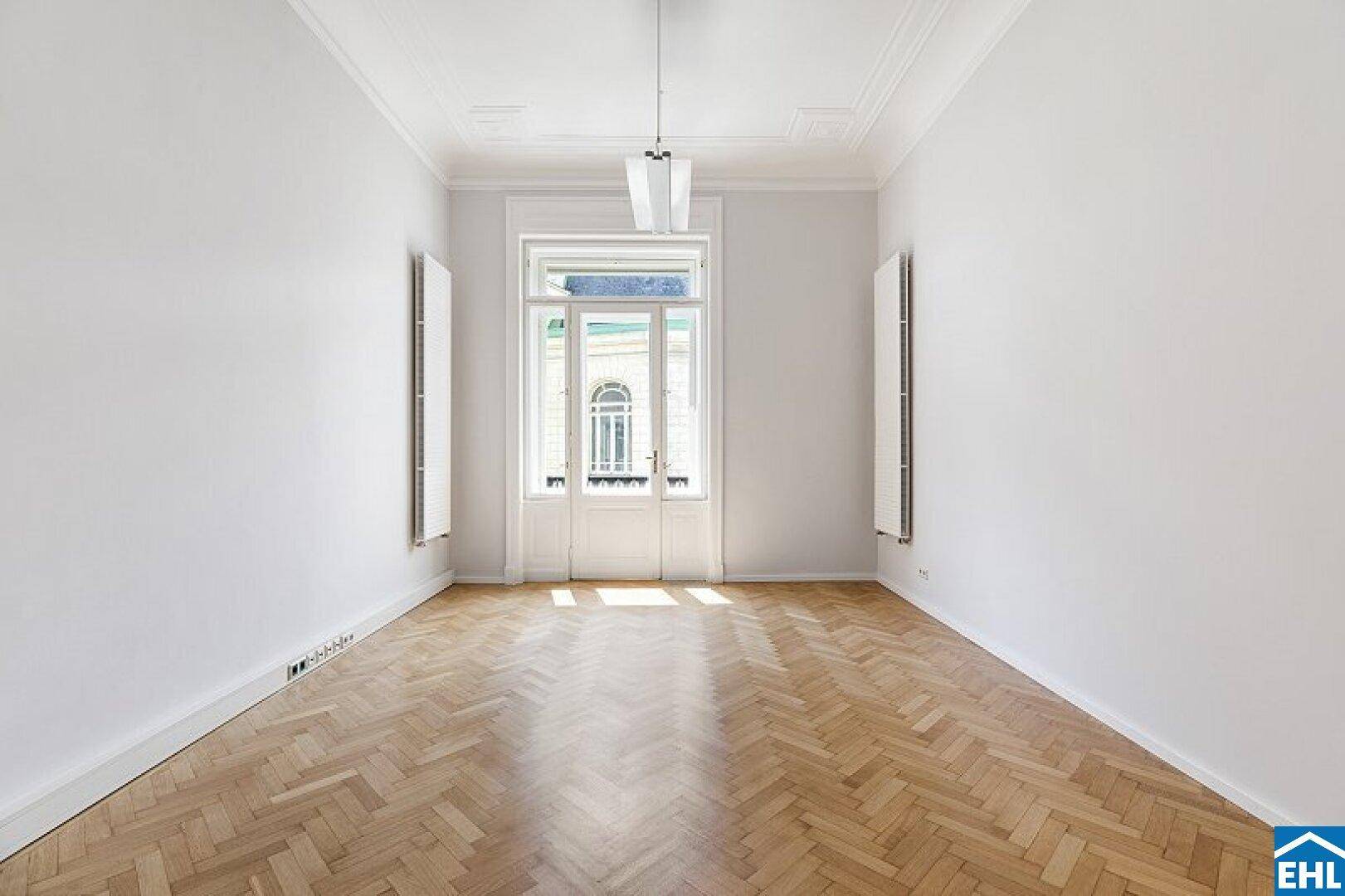 Heller, unmöblierter Raum mit Fischgrätparkett, hohen Decken und einem großen Fenster.