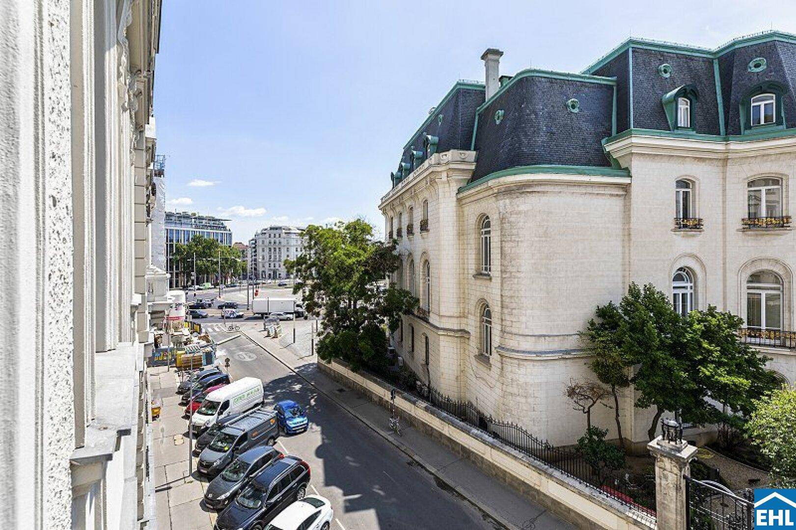 Blick auf die Straße mit parkenden Autos und einem historischen Gebäude mit Mansarddach.