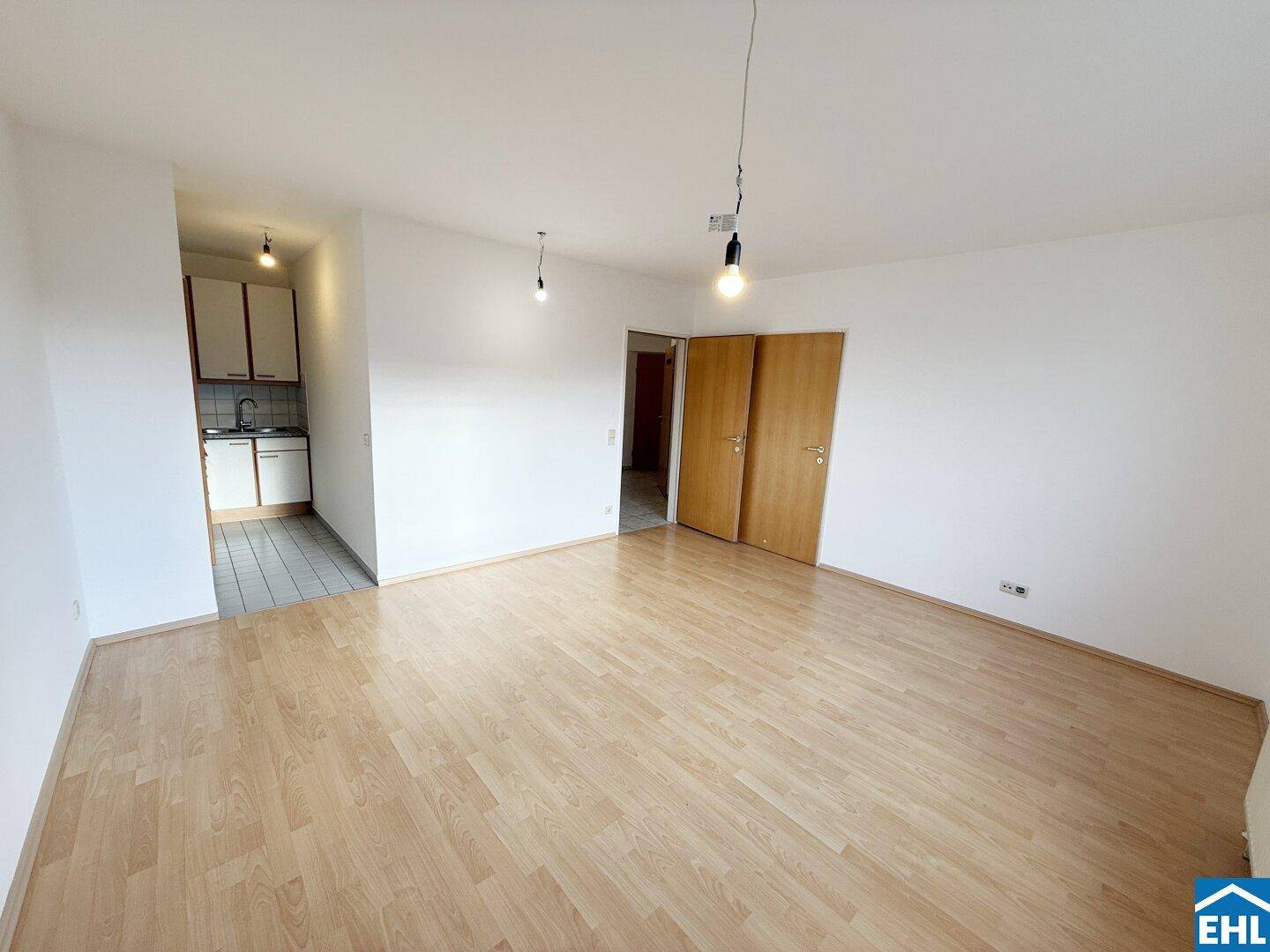 Geräumiges Wohnzimmer mit Parkettboden und einem Blick auf die angrenzende Kochnische.