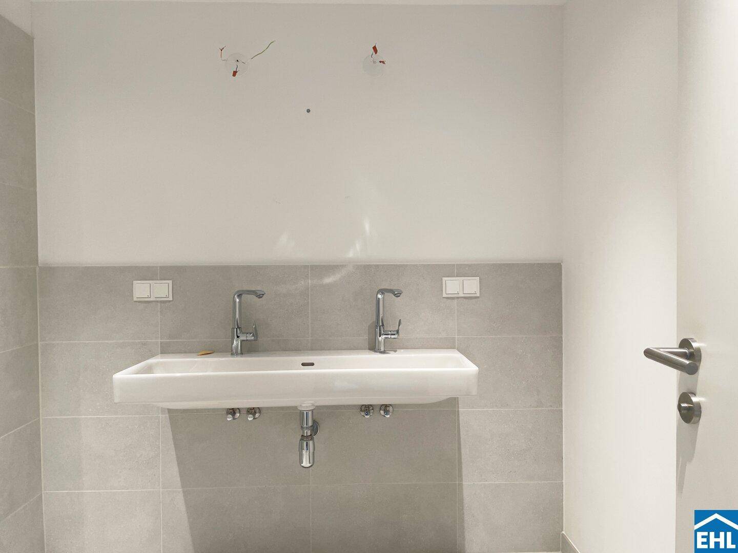 Doppelwaschbecken mit modernen Armaturen und hellgrauen Fliesen in einem Badezimmer.