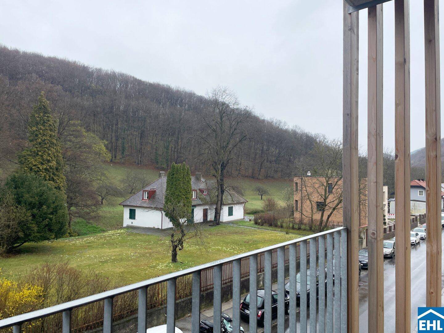 Ausblick vom Balkon auf eine grüne Hügellandschaft mit Häusern und einer Straße.