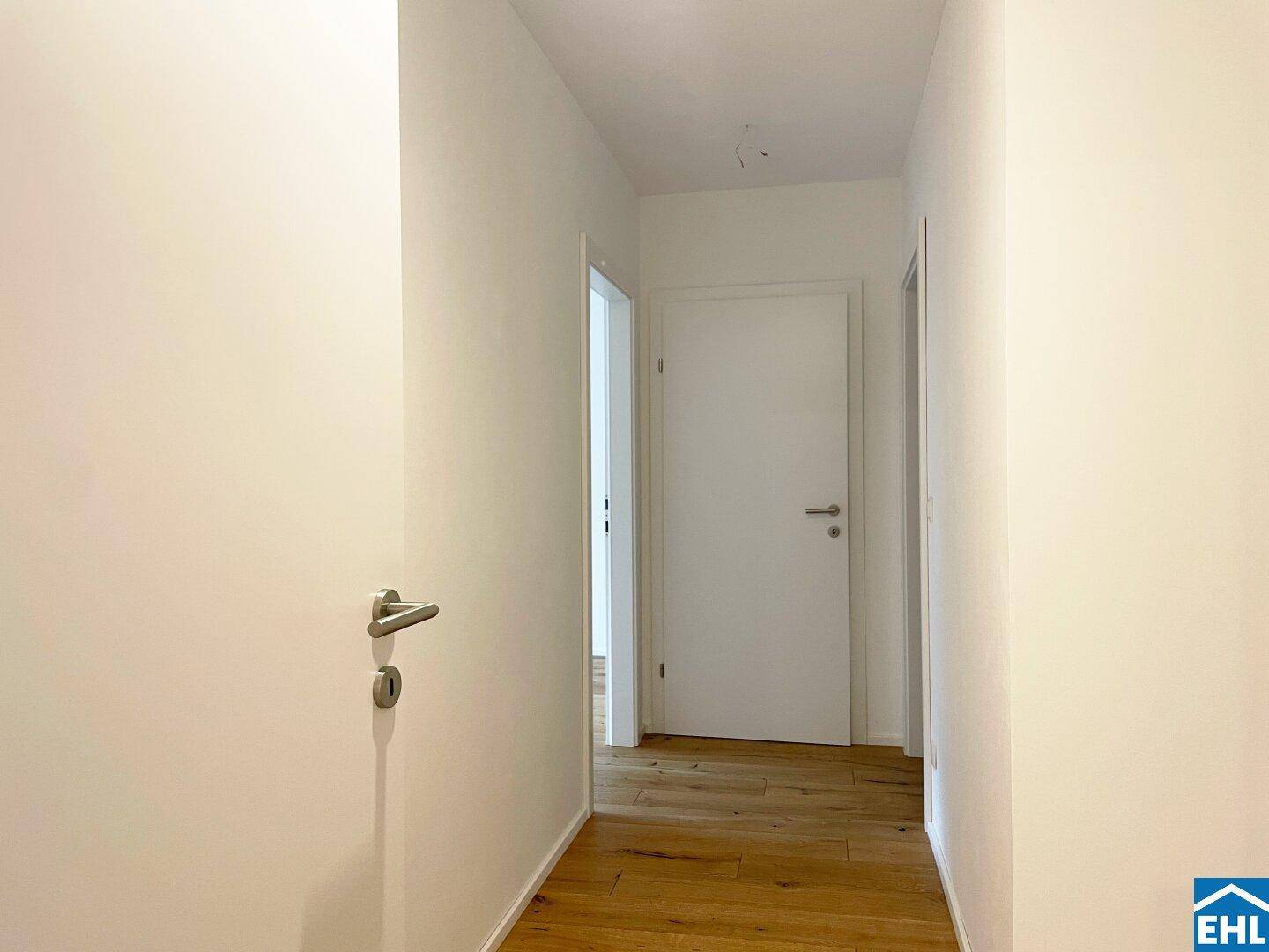 Heller Flur mit Holzboden und weißen Türen, der zu weiteren Räumen führt.
