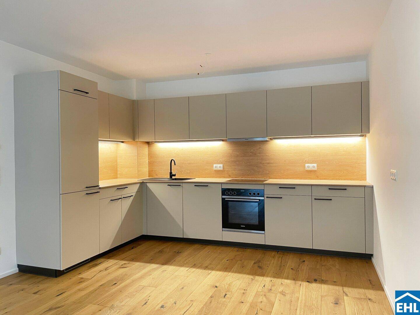 Moderne Einbauküche in L-Form mit hellen Fronten, Holzrückwand und integrierten Geräten.