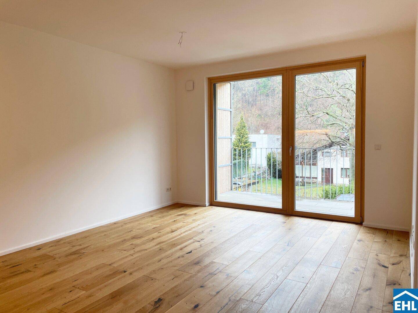 Heller Wohnraum mit Holzboden und großem Fenster, das Zugang zu einem Balkon bietet.