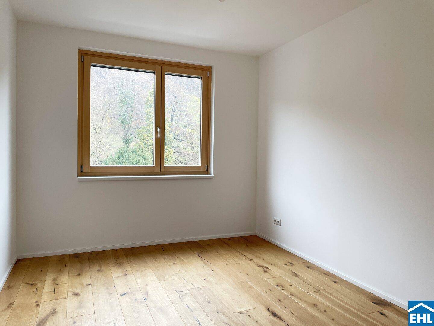 Schlafzimmer mit Holzboden und einem Fenster, das viel Tageslicht hereinlässt und Blick ins Grüne bietet.