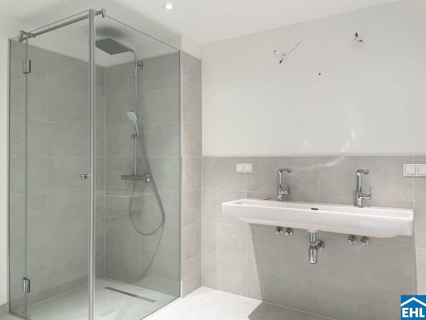 Modernes Badezimmer mit großer Glasdusche, Doppelwaschbecken und hellgrauen Fliesen.