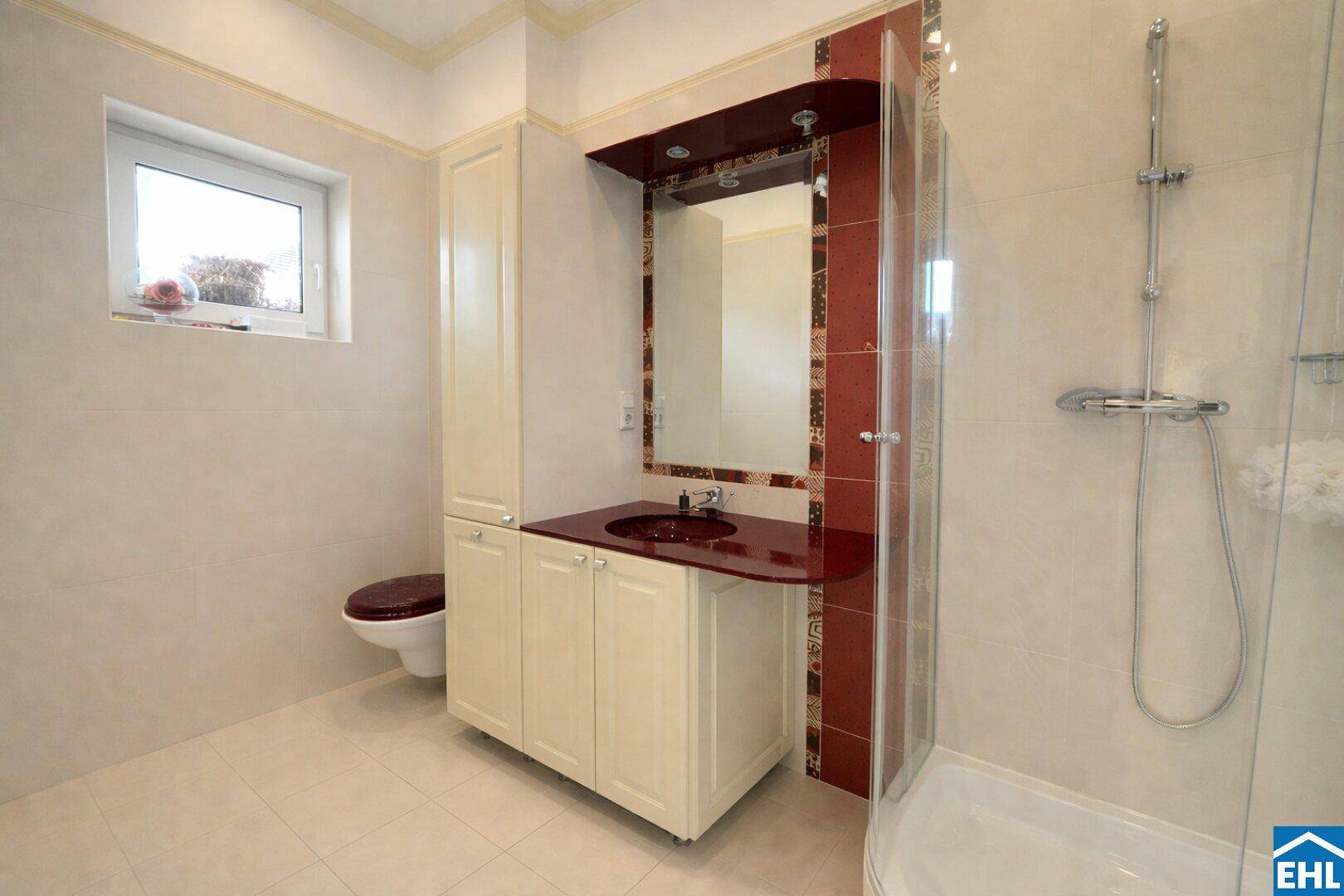 Modernes Badezimmer mit Dusche, Fenster und elegantem Waschtisch mit roter Akzentfarbe.