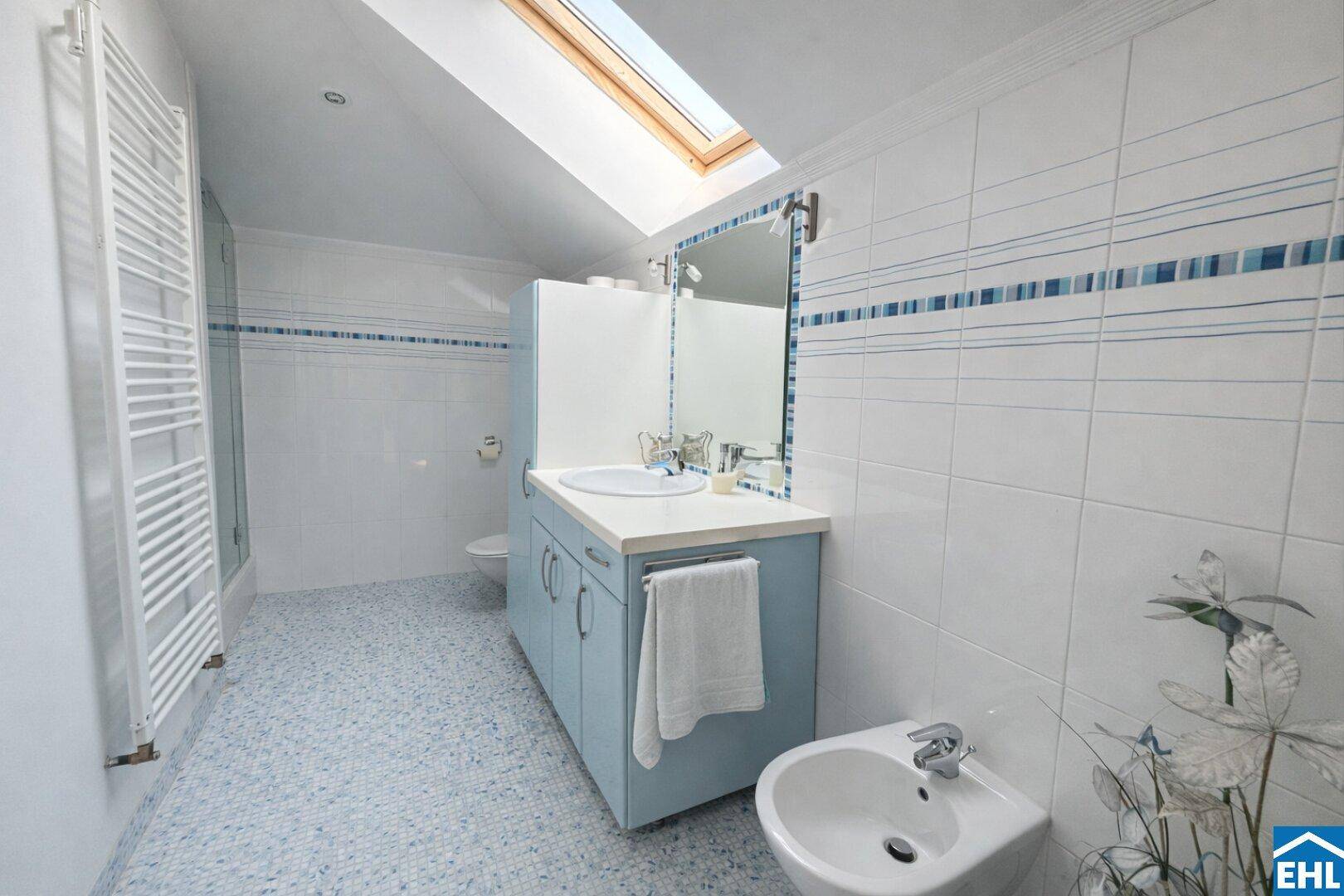 Helles Badezimmer mit Bidet, Waschtisch, Dachfenster und blauen Akzentfliesen.