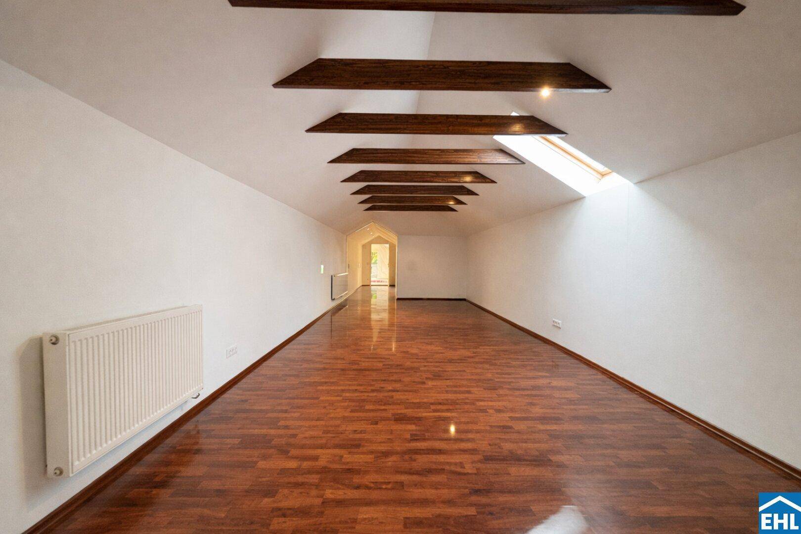 Langer, heller Dachbodenraum mit sichtbaren Holzbalken und glänzendem Parkettboden.