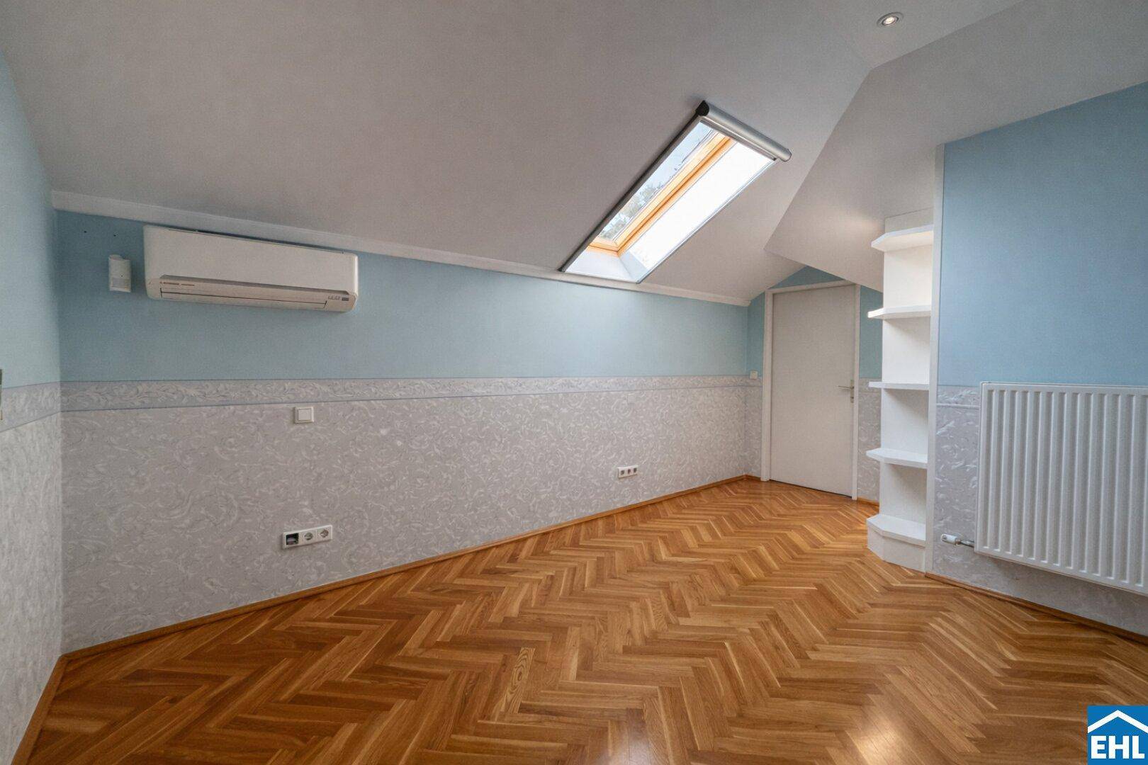 Dachgeschosszimmer mit blauer Wandgestaltung, Parkettboden und einem großen Dachfenster.
