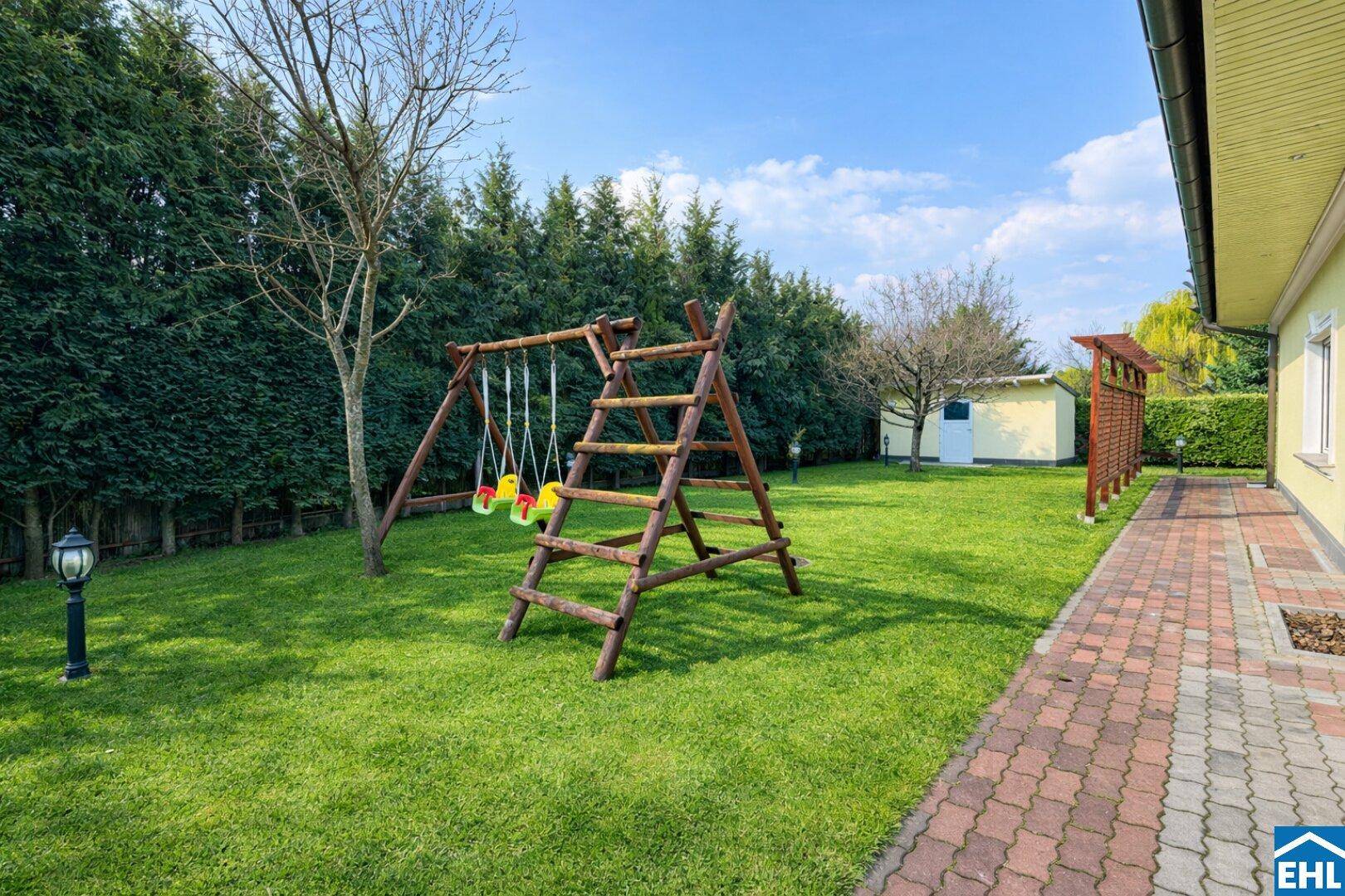 Großer Garten mit Kinderspielplatz, hohen Hecken und einem Gartenhaus im Hintergrund.