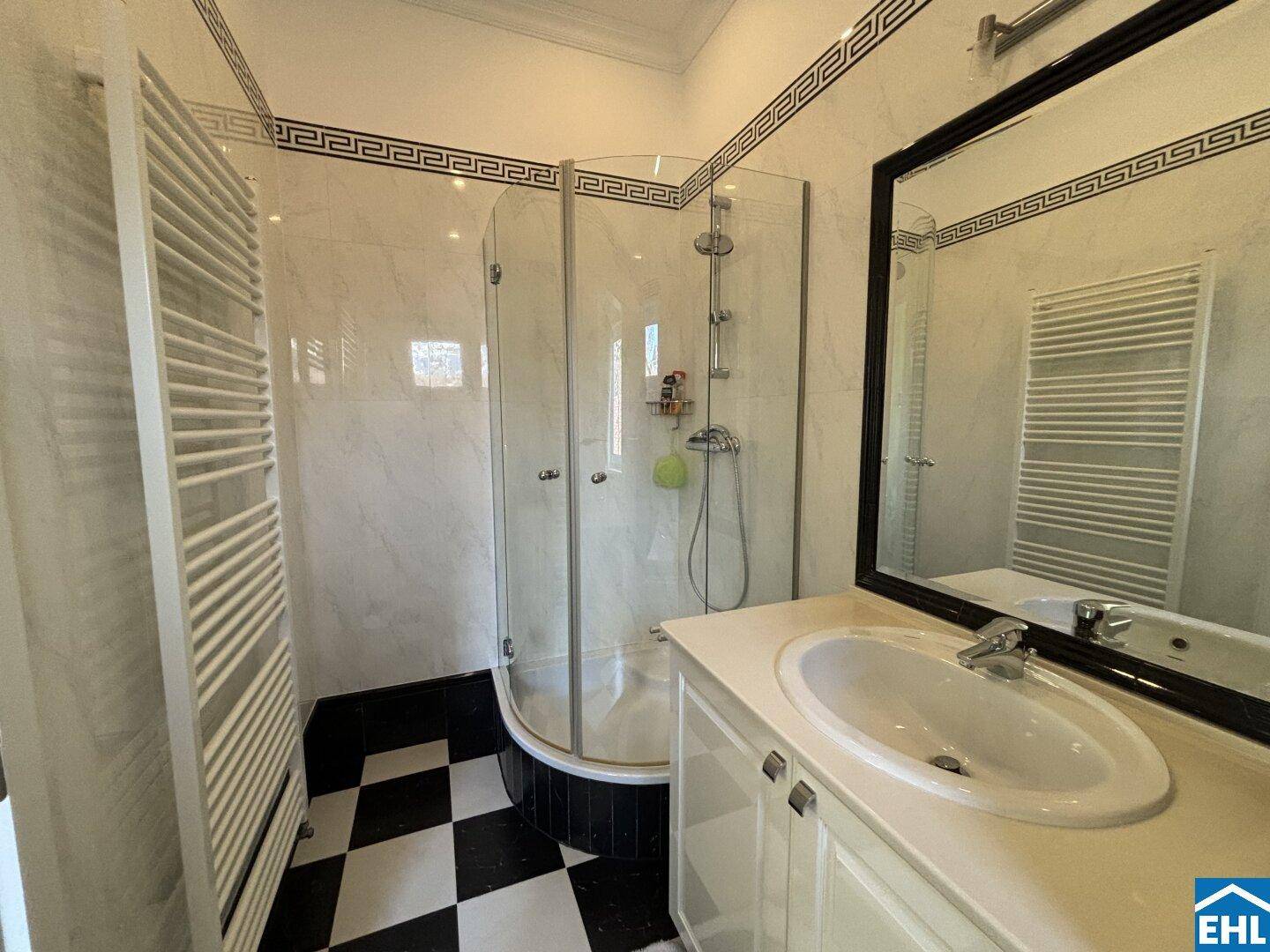 Badezimmer mit Dusche, Waschtisch und markantem schwarz-weißem Fliesenboden.