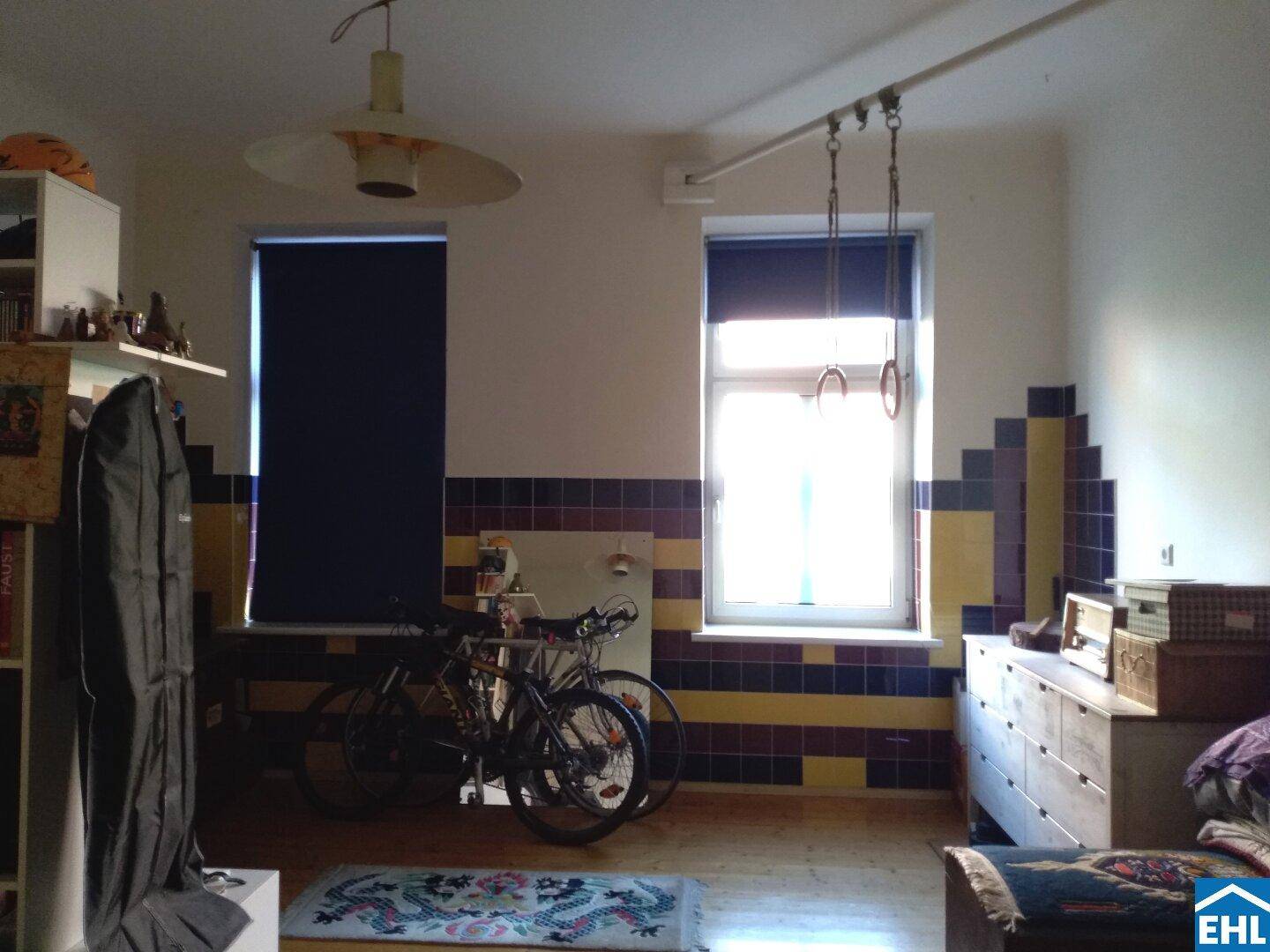 Helles Schlafzimmer mit zwei Fenstern, Holzboden und farbigen Wandfliesen, bietet viel Tageslicht.