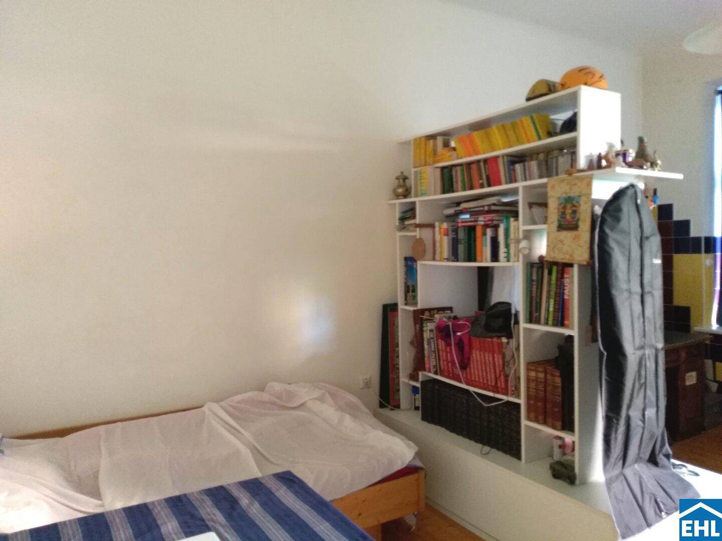 Gemütliches Schlafzimmer mit Holzboden und einem großen Bücherregal, das viel Stauraum bietet.