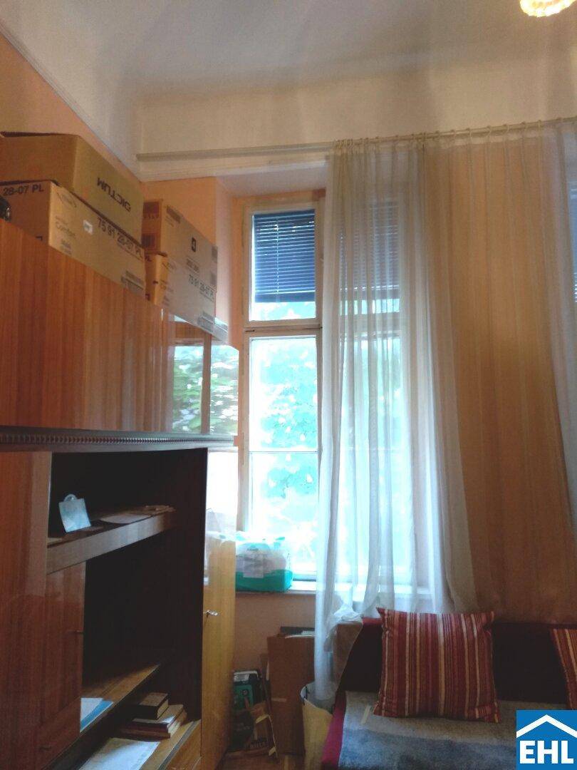 Detailansicht eines Fensters mit Vorhängen und einem Regal voller Kartons in einem Wohnraum.