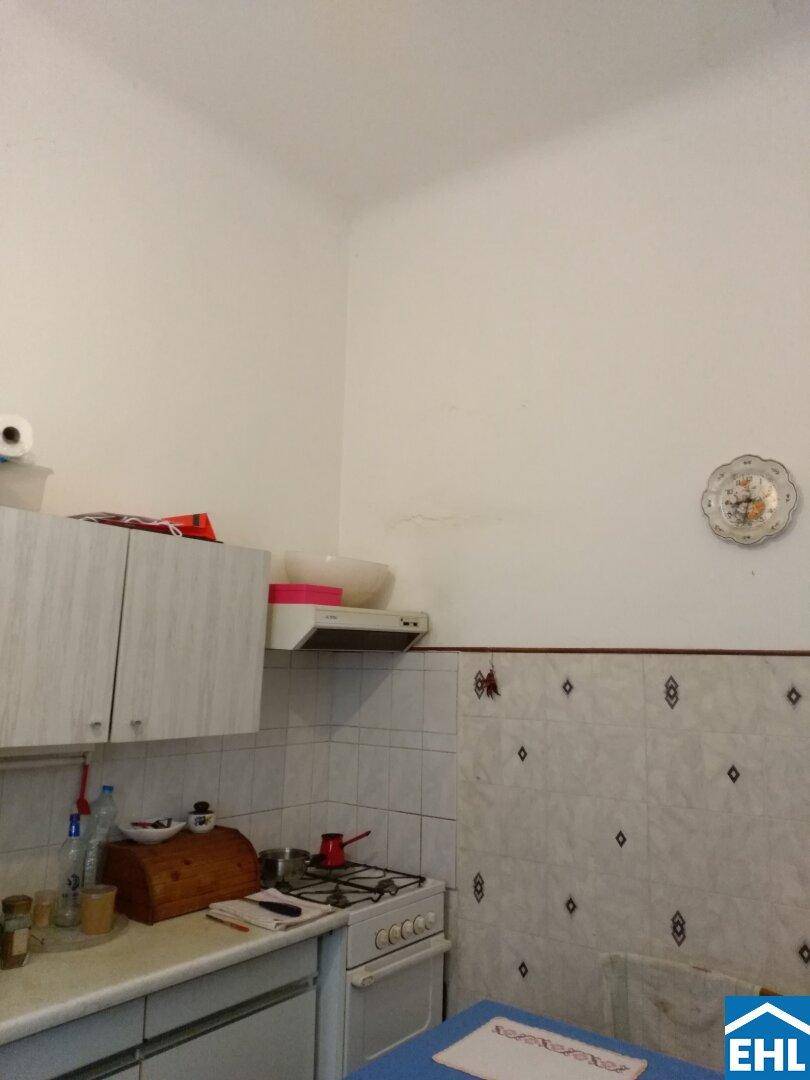 Kleine Küche mit Gasherd, Dunstabzugshaube und weißen Fliesen an der Wand.
