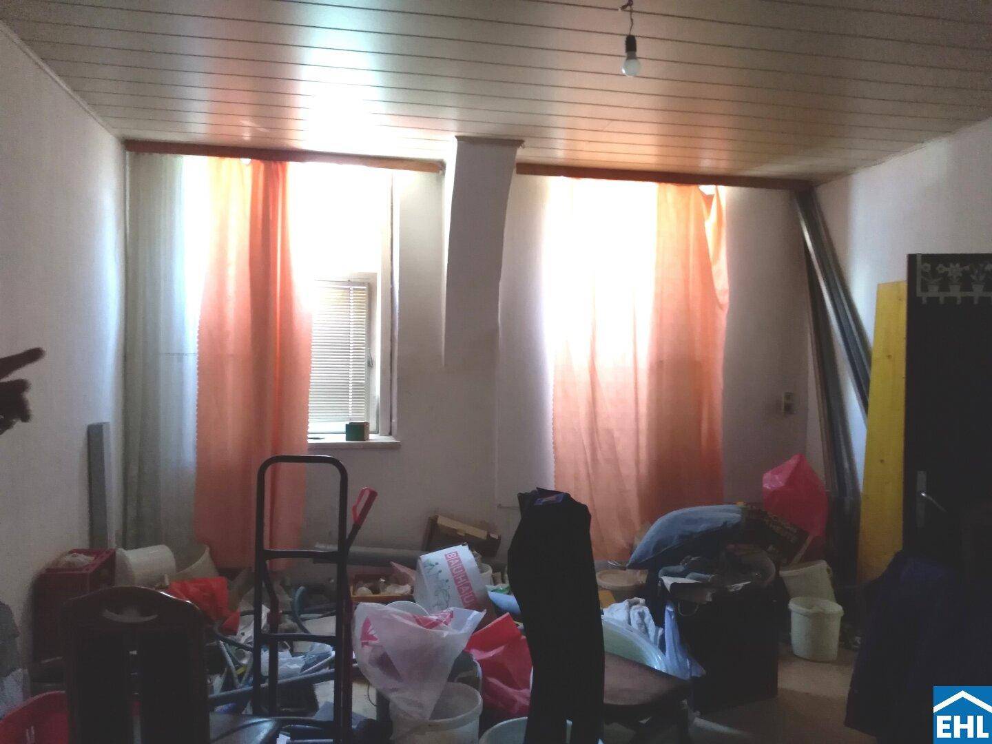 Ein unordentlicher Innenraum mit zwei Fenstern, die Tageslicht hereinlassen, und einer Holzpaneeldecke.