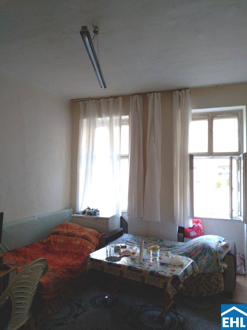 Heller Wohnraum mit mehreren Fenstern, Vorhängen und einfacher Einrichtung.