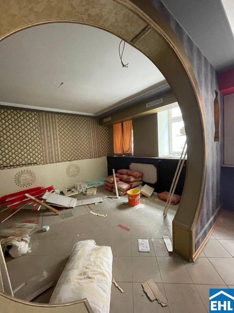 Renovierungsbedürftiger Raum mit Baumaterialien, gemusterter Tapete und einem dekorativen Bogen.