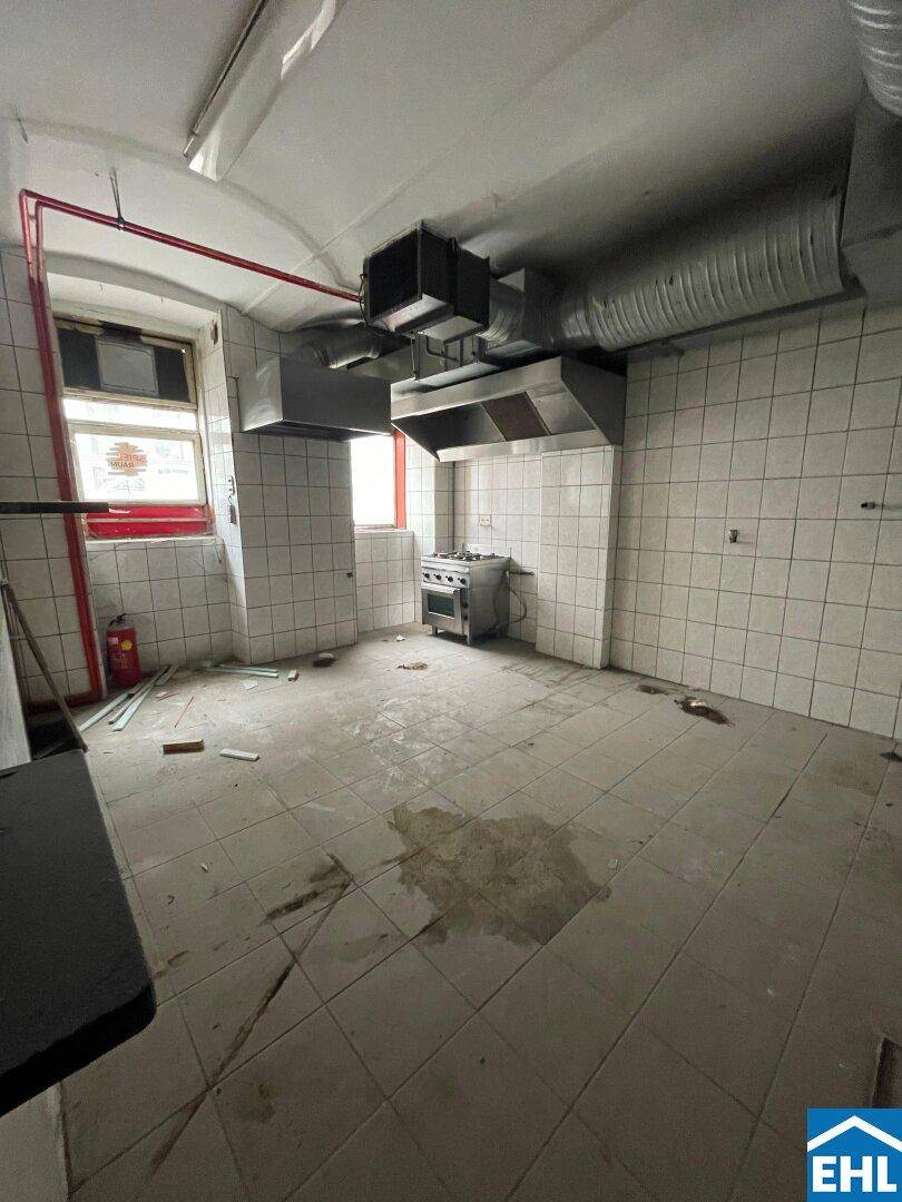 Gewerbliche Küche mit weißen Fliesenwänden, industriellen Dunstabzugshauben und einem Gasherd.